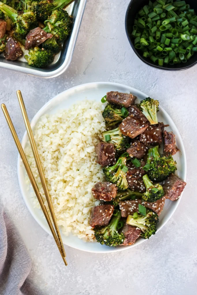 Sheet Pan Beef and Broccoli plated on a round white plate with gold chopsticks