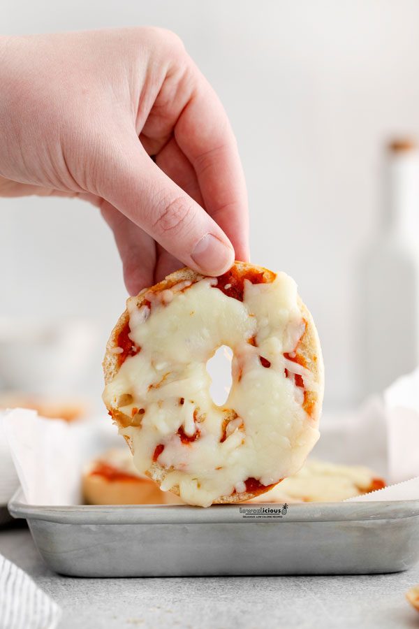 a hand holding up a low calorie pizza bagel topped with pizza sauce and melted mozzarella cheese