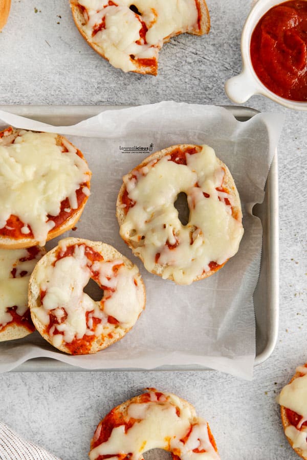 overhead shot of low calorie pizza bagels in a parchment paper lined quarter sheet pan