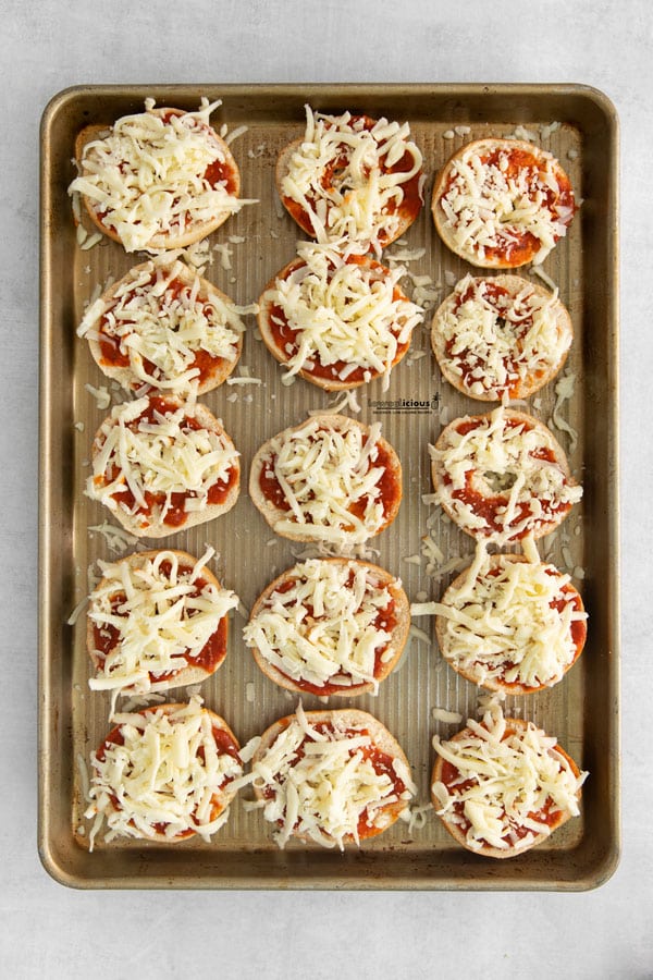 mini bagels on a half sheet pan halved and topped with pizza sauce and mozzarella cheese to make bagel pizzas