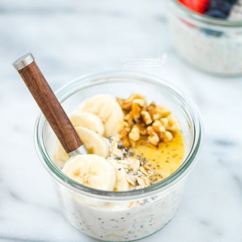 A bowl of overnight oats in a glass Weck jar with a wood handled spoon sticking out. The oats are topped with sliced banana, chopped walnuts, chia seeds, raw oats, and honey. Made from the recipe How to Make Overnight Oats.