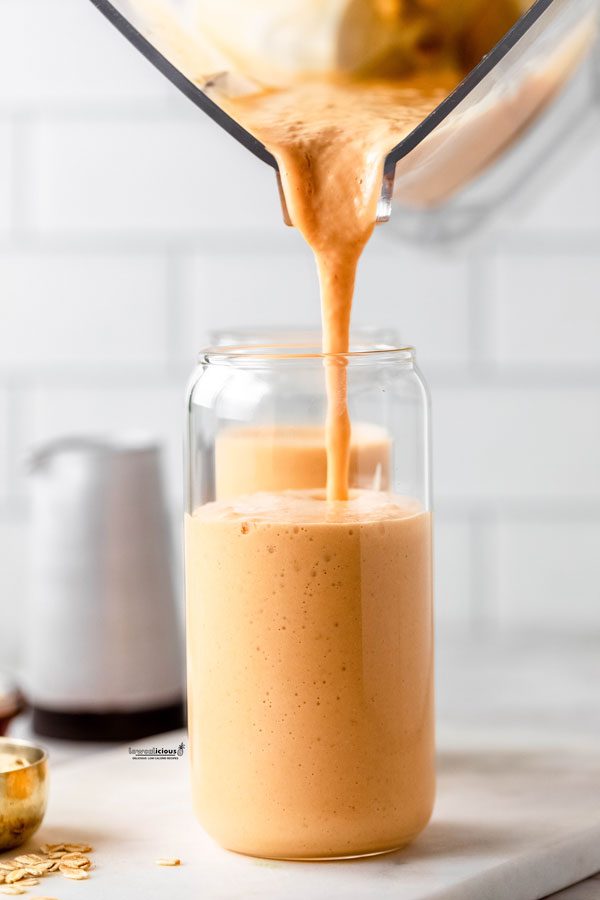 a blender canister being used to pour a pumpkin smoothie into a tall clear glass