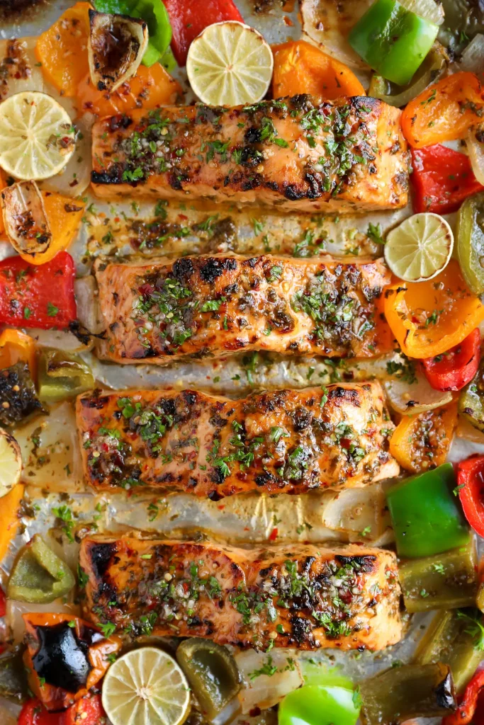 overhead shot of a baked salmon sheet pan dinner with sliced limes and a variety of color bell peppers