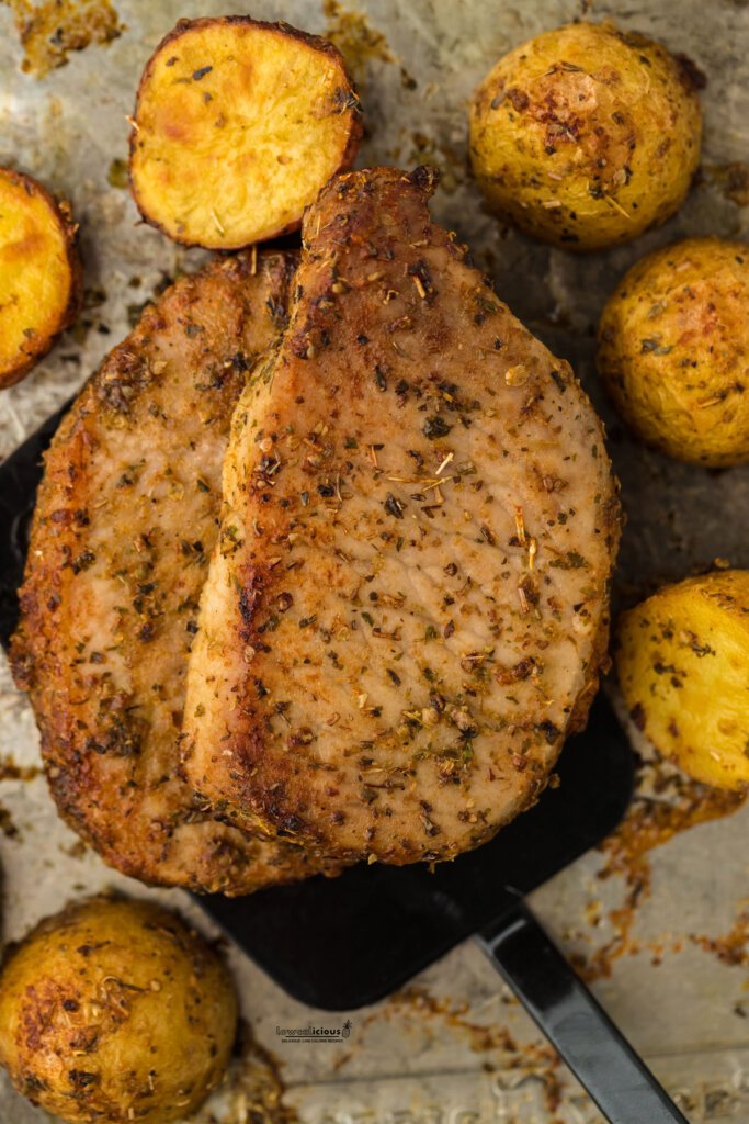 baked Ranch Pork Chops on a sheet pan with roasted potatoes being removed from the pan with a black spatula