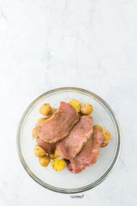 boneless pork chops and halved baby potatoes tossed with dry seasoning and oil in a large glass bowl