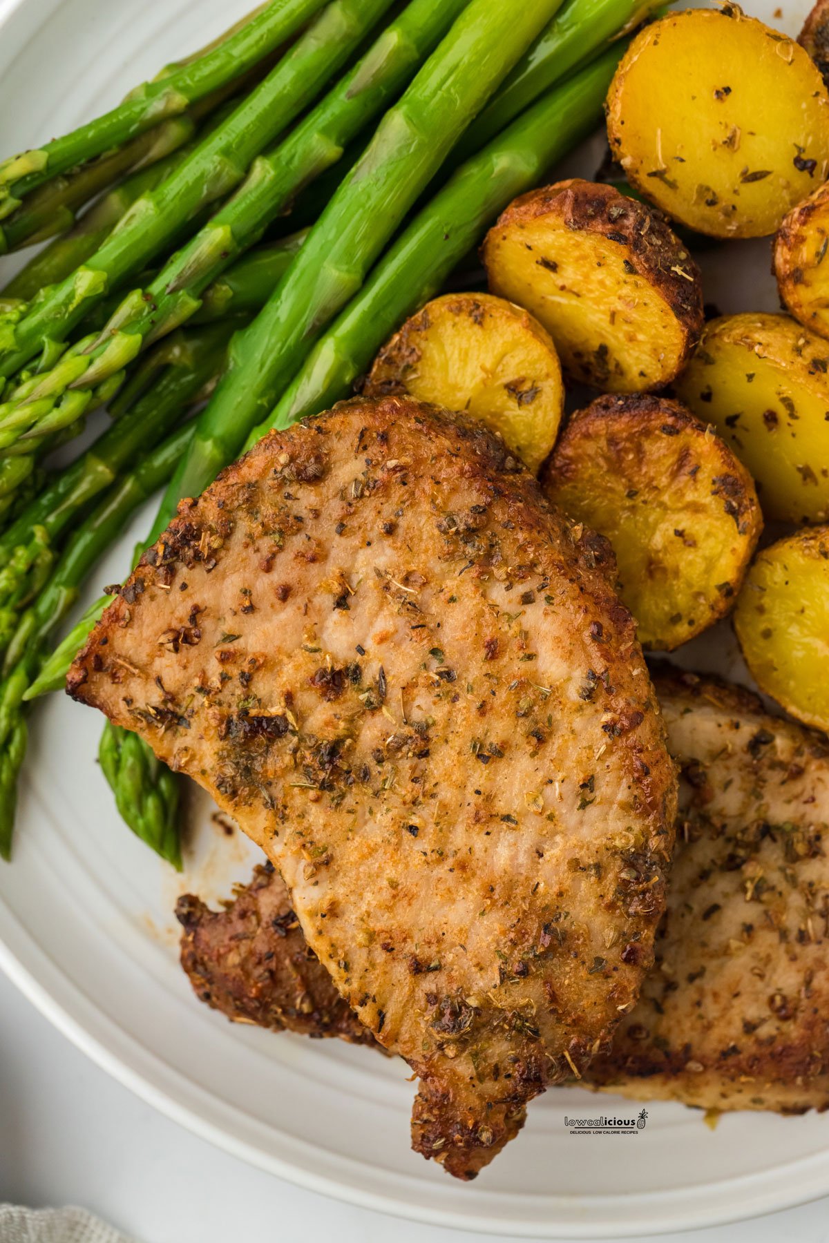 baked ranch pork chops on a white plate with roasted potatoes and steamed asparagus