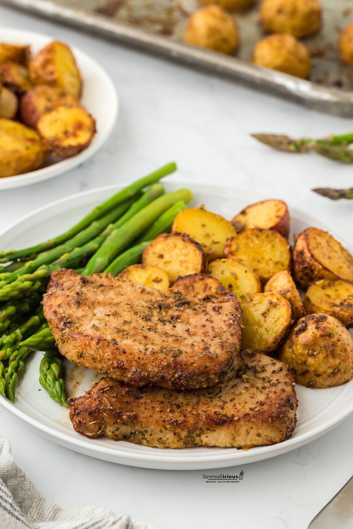 cooked and plated Sheet Pan Ranch Pork Chops with Crispy Potatoes on a round white plate with steamed asparagus