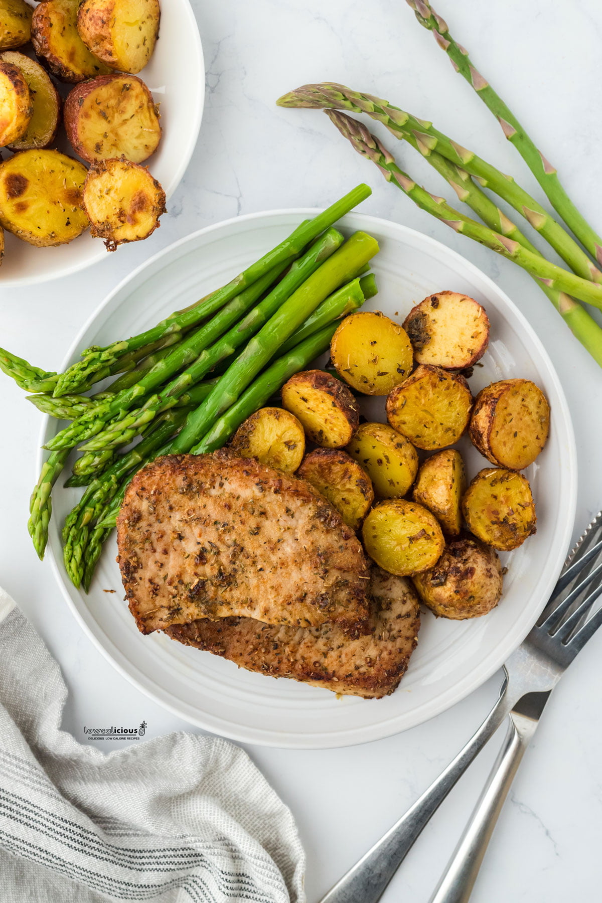 cooked and plated Sheet Pan Ranch Pork Chops with Crispy Potatoes on a round white plate with steamed asparagus