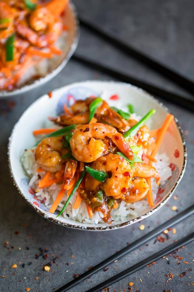 honey garlic shrimp in a small white bowl over rice with julienned carrots and scallions