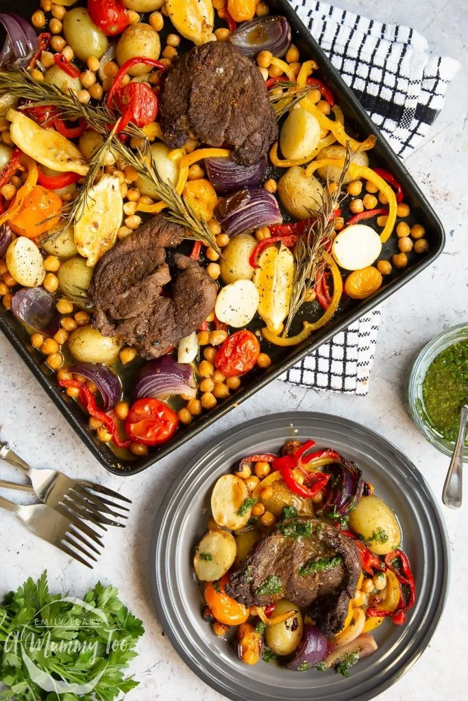 overhead shot of Succulent Lamb Steak And Vegetable Sheet Pan Meal with some on the sheet pan and some on a round gray plate