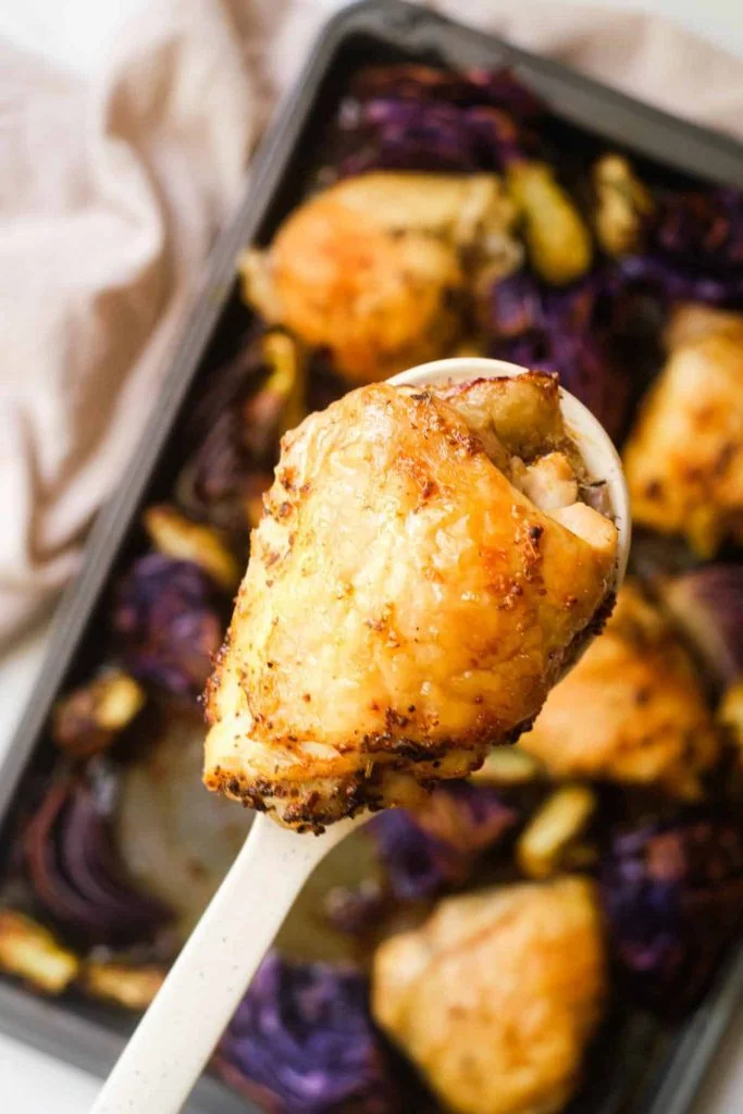 overhead shot of Sheet Pan Chicken Thigh on a serving spoon above Brussels Sprouts and Cabbage