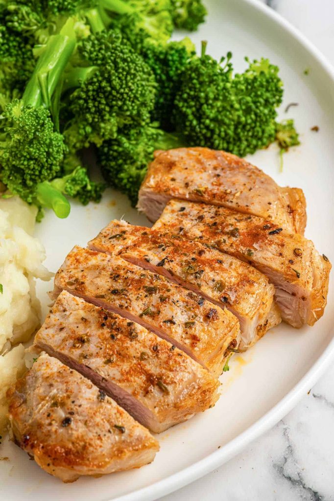 sliced Air Fried Pork Chops on a white plate with steamed broccoli and mashed potatoes