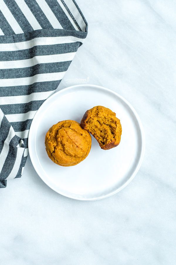 2 Low Calorie Pumpkin Muffins with Cake Mix on a small white plate. 1 has a bite taken out