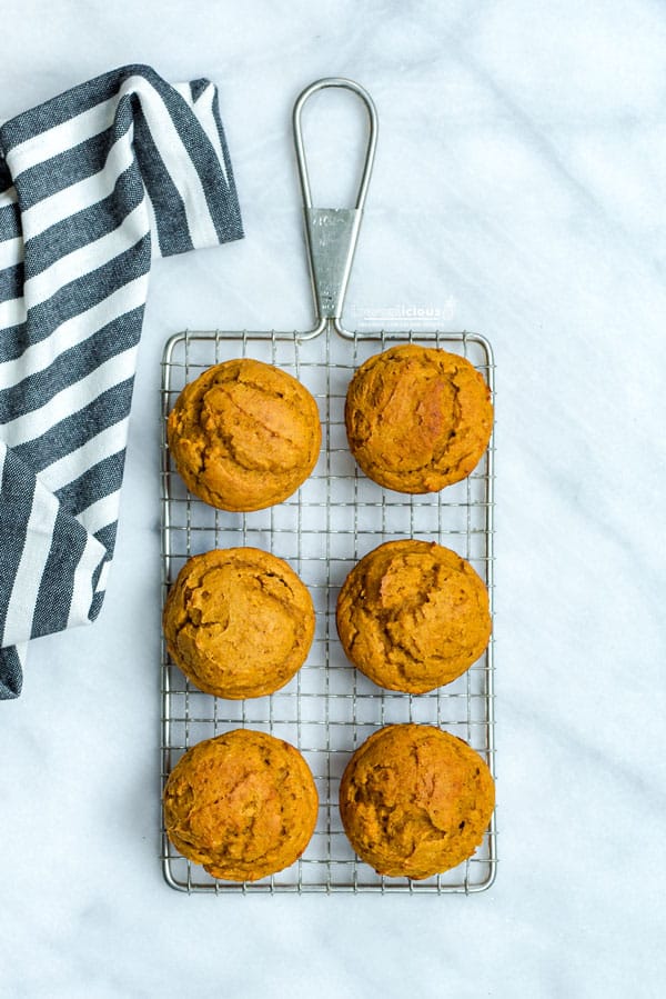 overhead shot of 6 Low Calorie Pumpkin Muffins with Cake Mix on a small wire rack with a black and white striped kitchen towel next to it