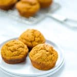 3 Low Calorie Pumpkin Muffins with Cake Mix on a stack of 2 small white plates with more muffins in the background