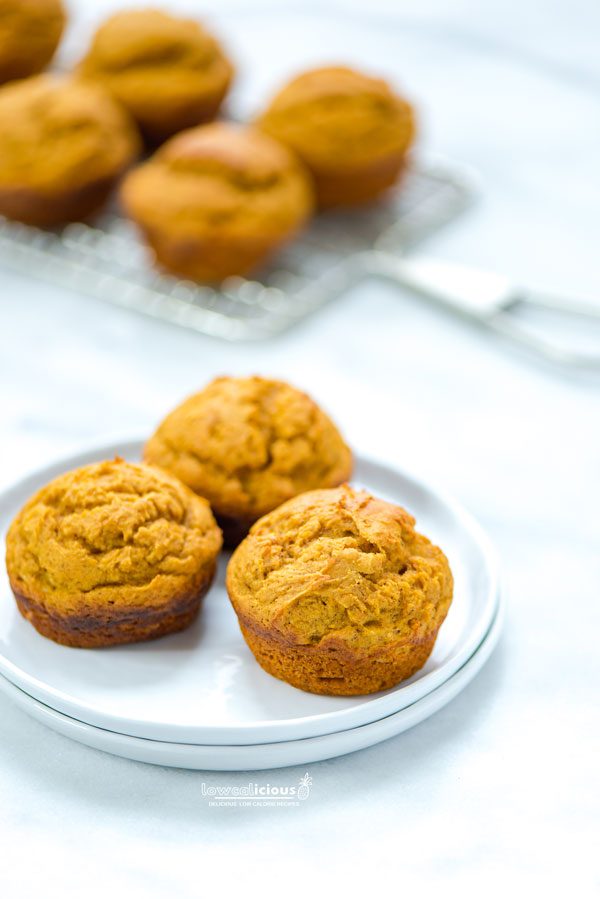 3 Low Calorie Pumpkin Muffins with Cake Mix on a stack of 2 small white plates with more muffins in the background