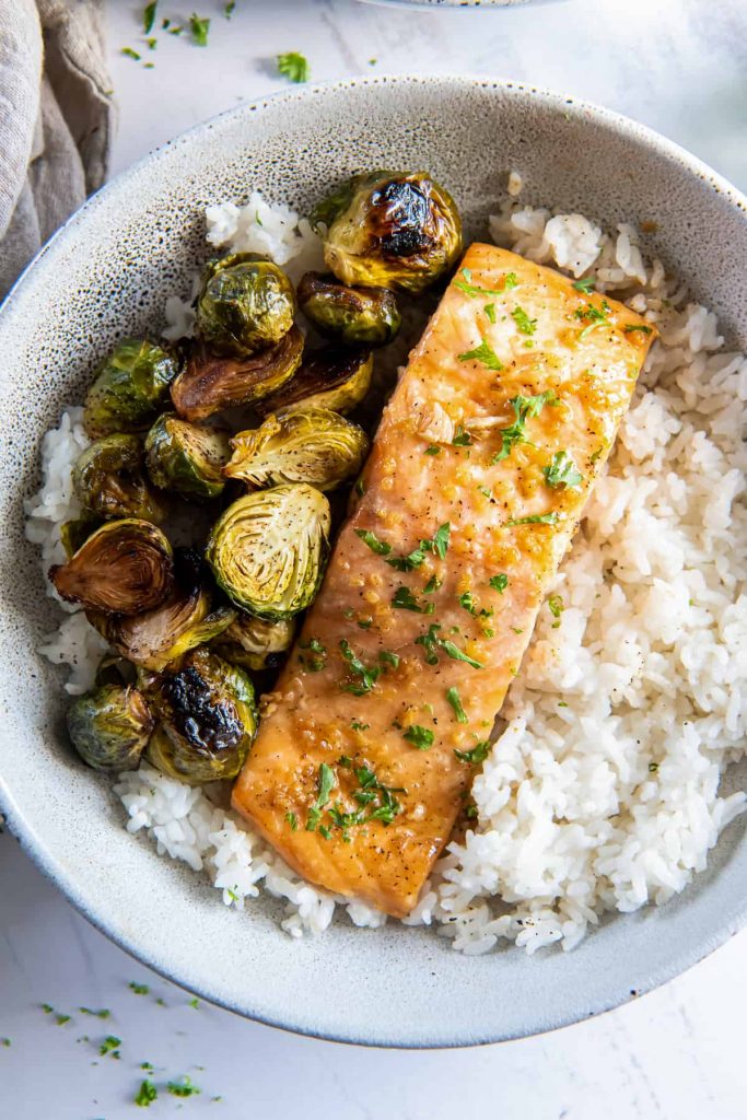 Oven Roasted Salmon with Maple Glaze in a white bowl on top of white rice with roasted Brussels sprouts