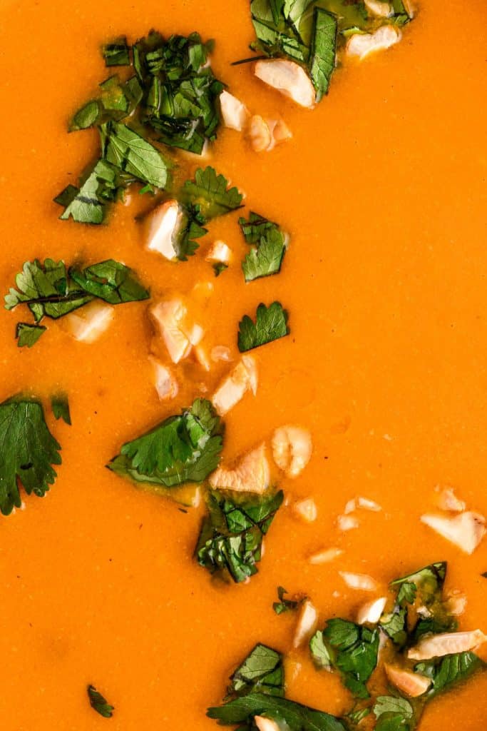 overhead closeup shot of Cashew Carrot Ginger Soup garnished with chopped cilantro and chopped cashews
