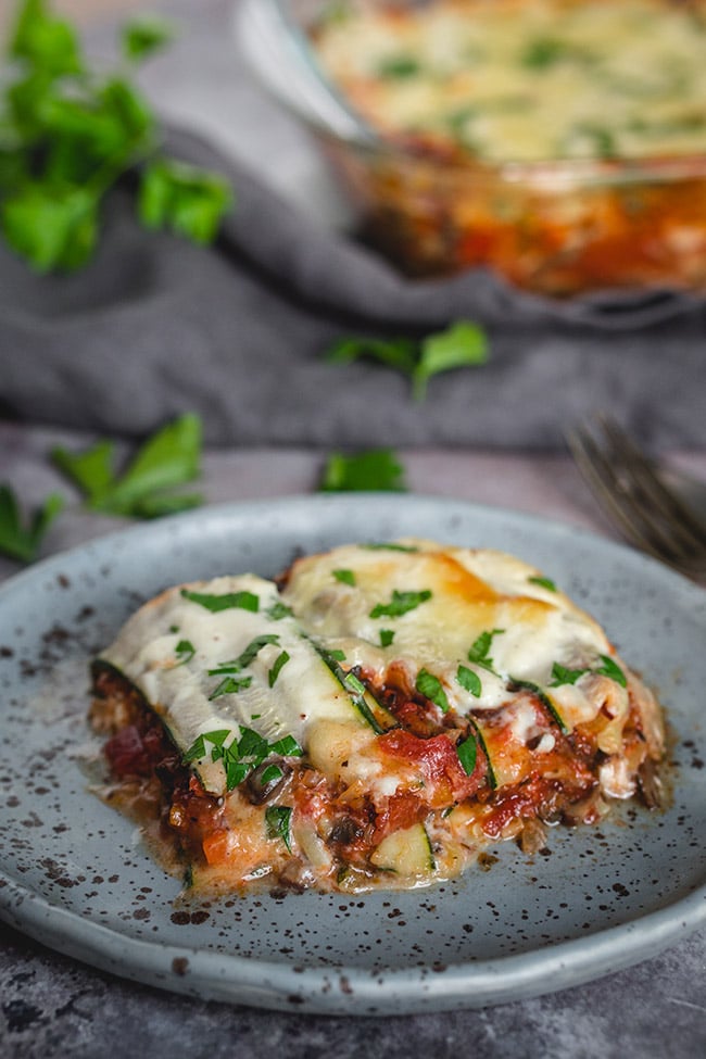 a slice of Vegetarian Zucchini Lasagna with Mushroom Bolognese on a small round blue plate garnished with fresh chopped parsley