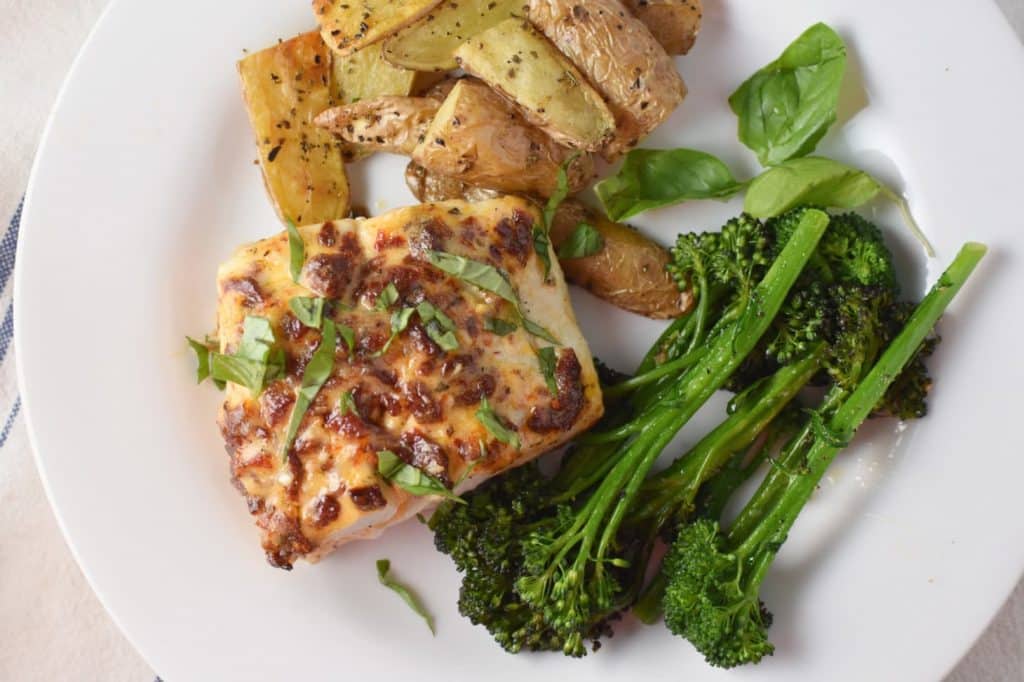 overhead shot of Mediterranean Baked Halibut on a white plate with broccolini and roasted potatoes