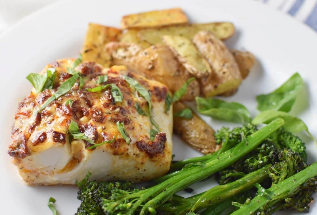 Mediterranean Baked Halibut on a white plate with broccolini and roasted potatoes
