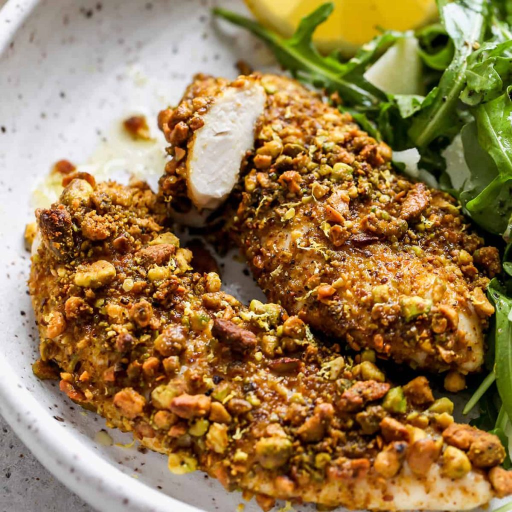 Pistachio Crusted Chicken Tenders on a small pottery plate with high sides with a wedge of lemon and arugula