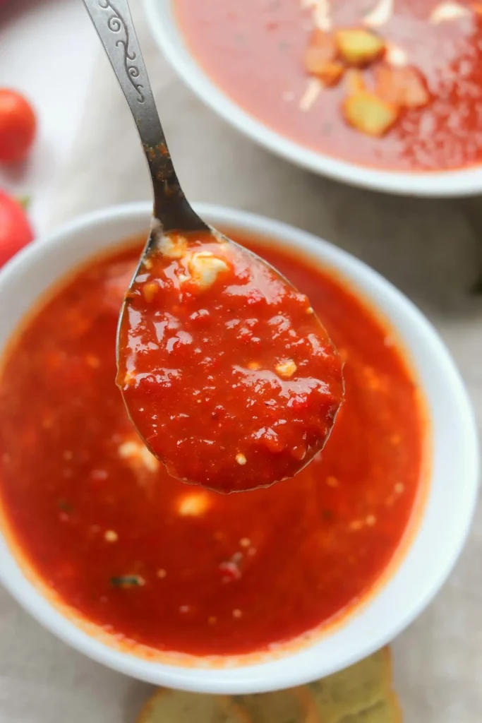 overhead shot of Roasted Red Pepper Tomato Soup on a silver soup spoon over a bowl of soup