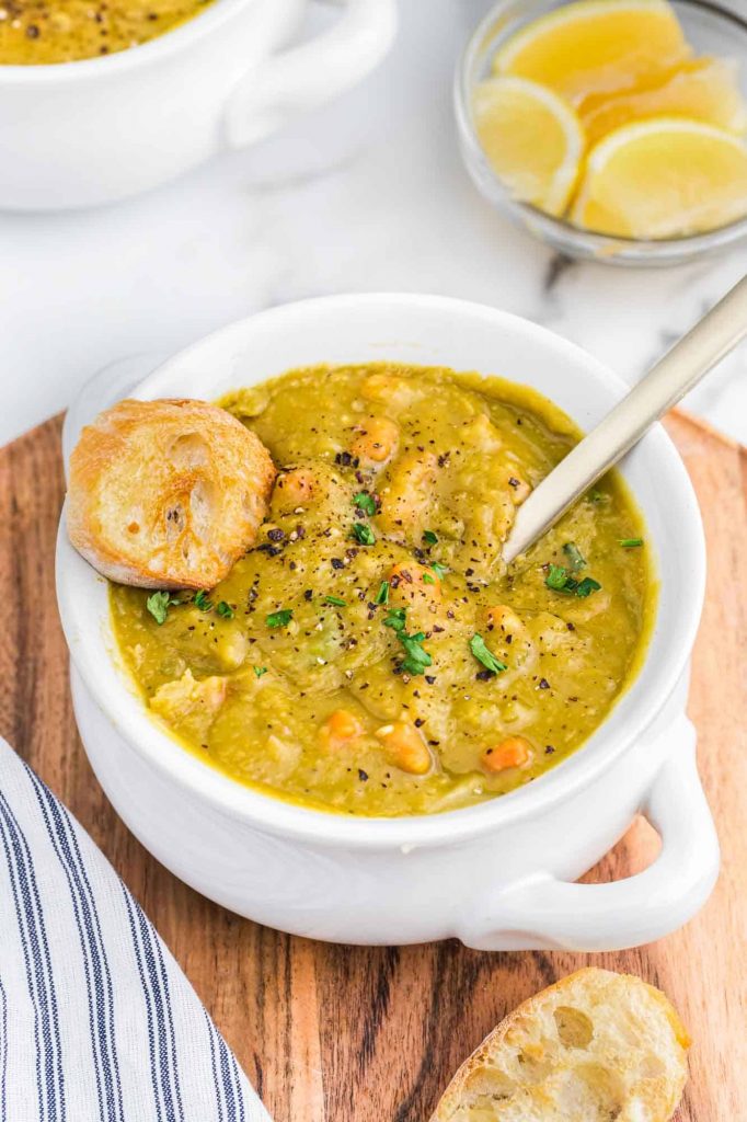 Instant Pot Split Pea Soup in a white bowl with a silver spoon garnished with a toasted piece of baguette