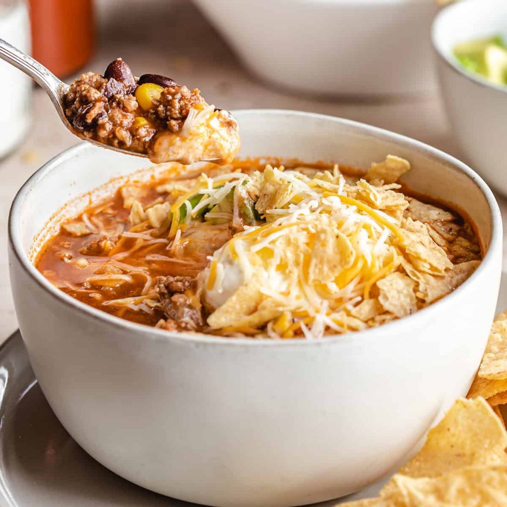 Slow Cooker Taco Soup in a white bowl topped with shredded cheese and sour cream with a spoon taking a spoonful