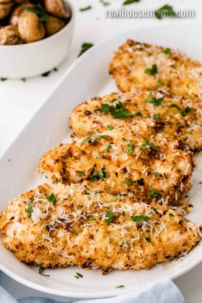 Cooked Air Fryer Parmesan Crusted Chicken on a large white serving tray garnished with chopped fresh parsley - one of the recipes from this week's healthy weekly meal plan