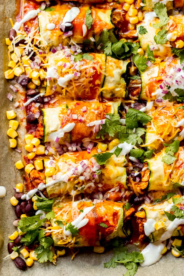 Cooked Zucchini Chicken Enchiladas on a sheet pan garnished with corn, cilantro, red onion, and sour cream - one of the recipes from this week's healthy weekly meal plan