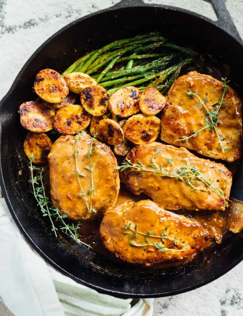 cooked Apricot Balsamic Pork Chops in a cast iron skillet with potatoes and asparagus - one of the recipes from this week's healthy weekly meal plan