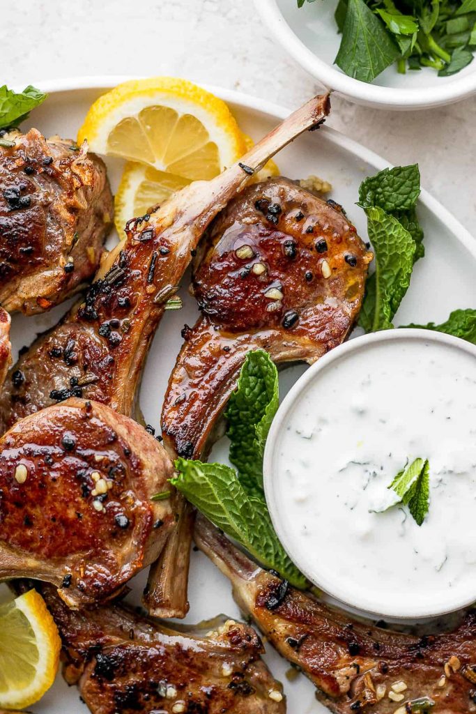 Grilled Lamb Chops on a white plate with greens and lemon wedges - one of the recipes for this week's healthy weekly meal plan
