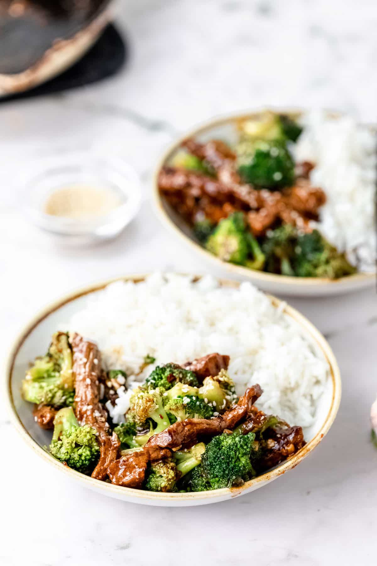 healthy beef and broccoli stir fry plated in two bowls with white rice on one half of each bowl