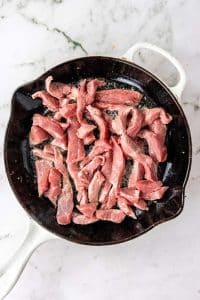 overhead shot of sliced beef cooking in a cast iron skillet to make a healthy beef and broccoli stir fry recipe