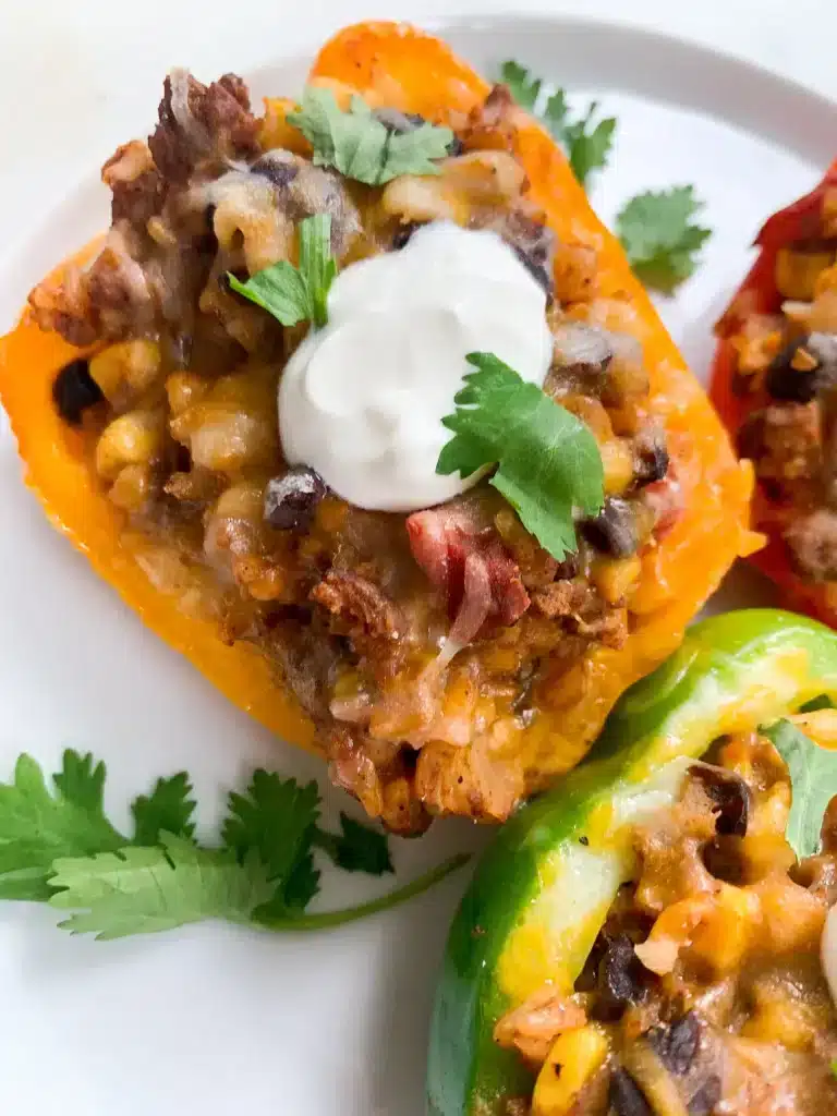 Taco Stuffed Peppers on a white plate garnished with sour cream and fresh cilantro. One of the recipes for this week's healthy weekly meal plan