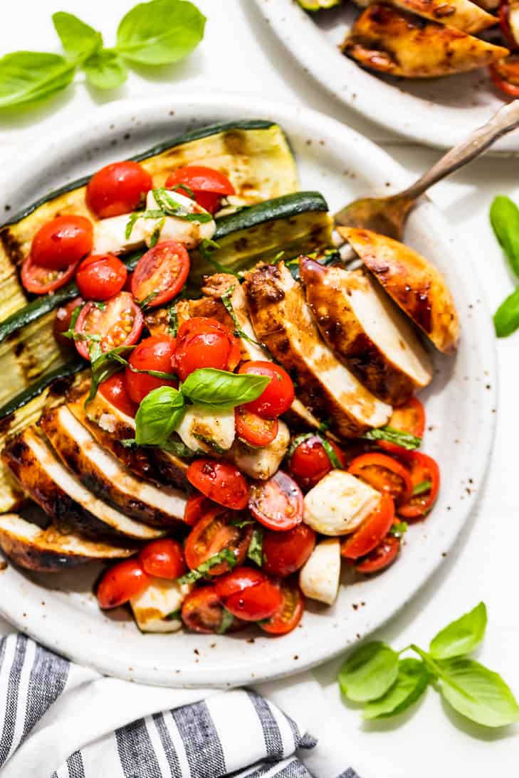 Overhead shot of grilled balsamic chicken breast sliced and plated with Caprese salad and zucchini - one of the recipes for this week's healthy weekly meal plan