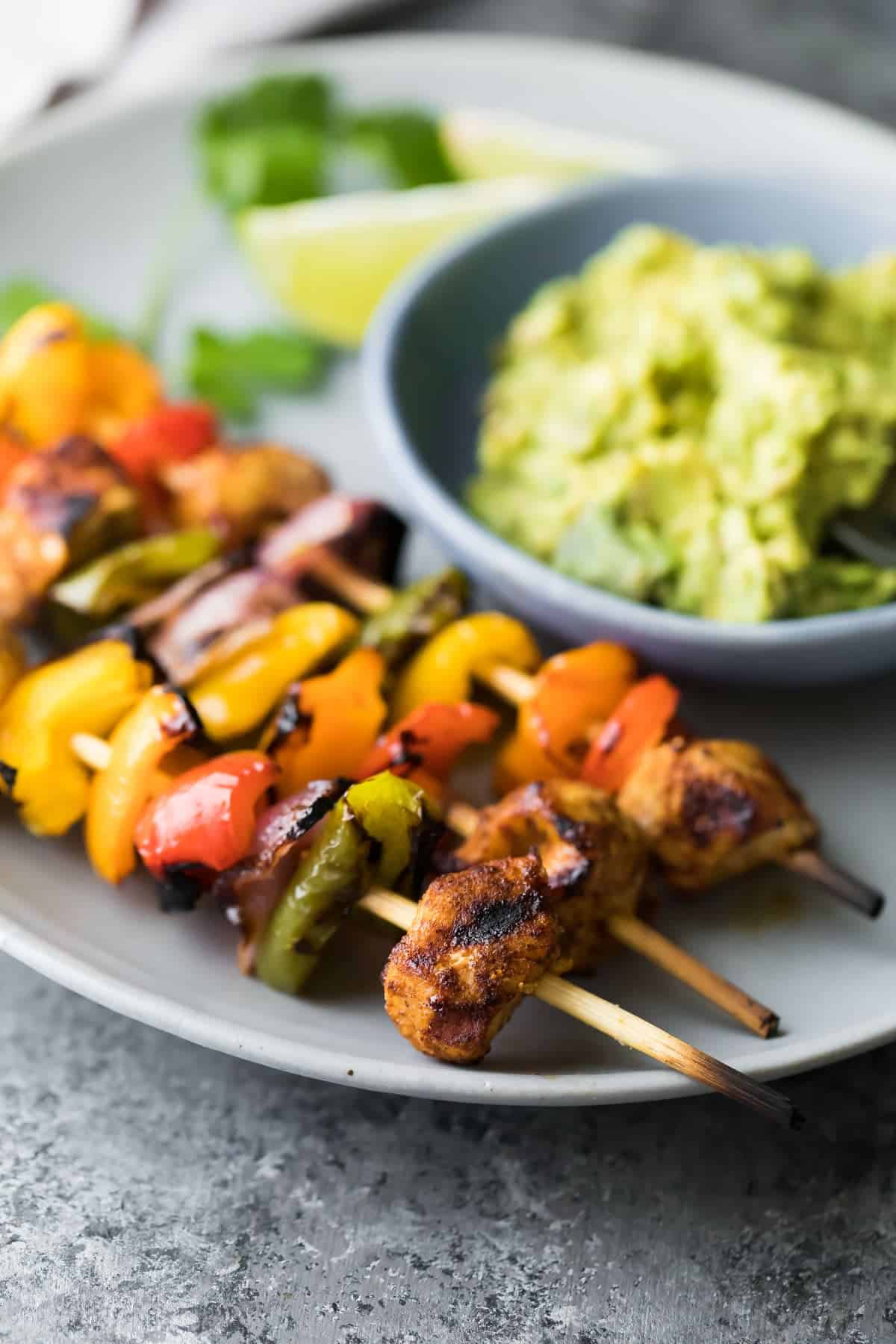 Grilled Chicken Fajita Skewers cooked and plated with wedges of lime and bowl of guacamole - one of the recipes for this week's healthy weekly meal plan
