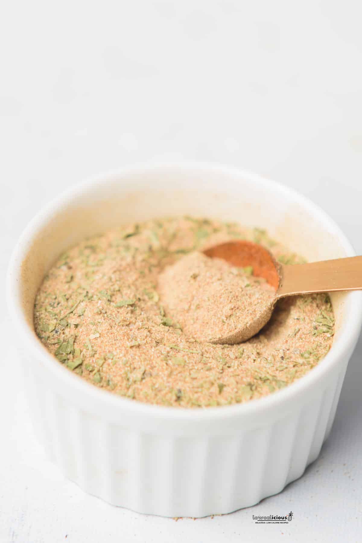 homemade chicken seasoning mixed together in a small white ramekin with a small copper measuring spoon