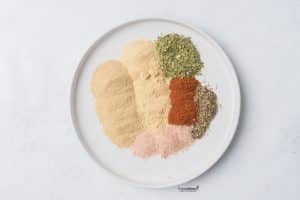 ingredients (individual spices) on a white plate to make a homemade chicken seasoning blend