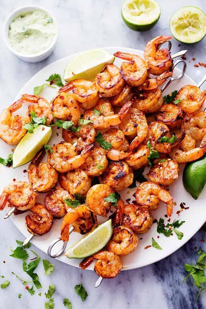 cooked grilled shrimp on skewers on a white serving plate garnished with chopped cilantro and lime wedges - one of the recipes for this week's healthy weekly meal plan