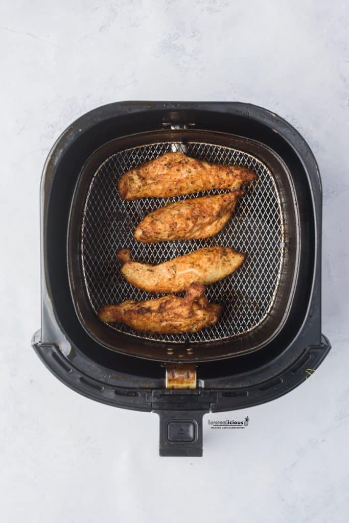 overhead shot of seasoned cooked chicken tenders in an air fryer basket for air fryer chicken tenders (no breading)
