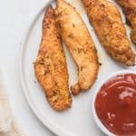 overhead shot of cooked air fryer chicken tenders (no breading) on a round white plate with a small bowl of ketchup