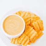 overhead shot of viral TikTok Cottage Cheese Queso Dip served in a small white bowl on top of a round white plate with some Sun Chips on the side