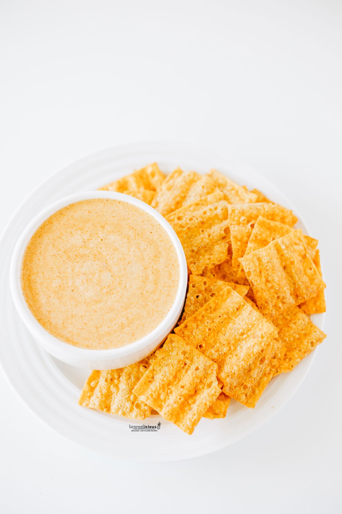 cottage cheese queso in a small white bowl on top of a round white plate with orange square chips