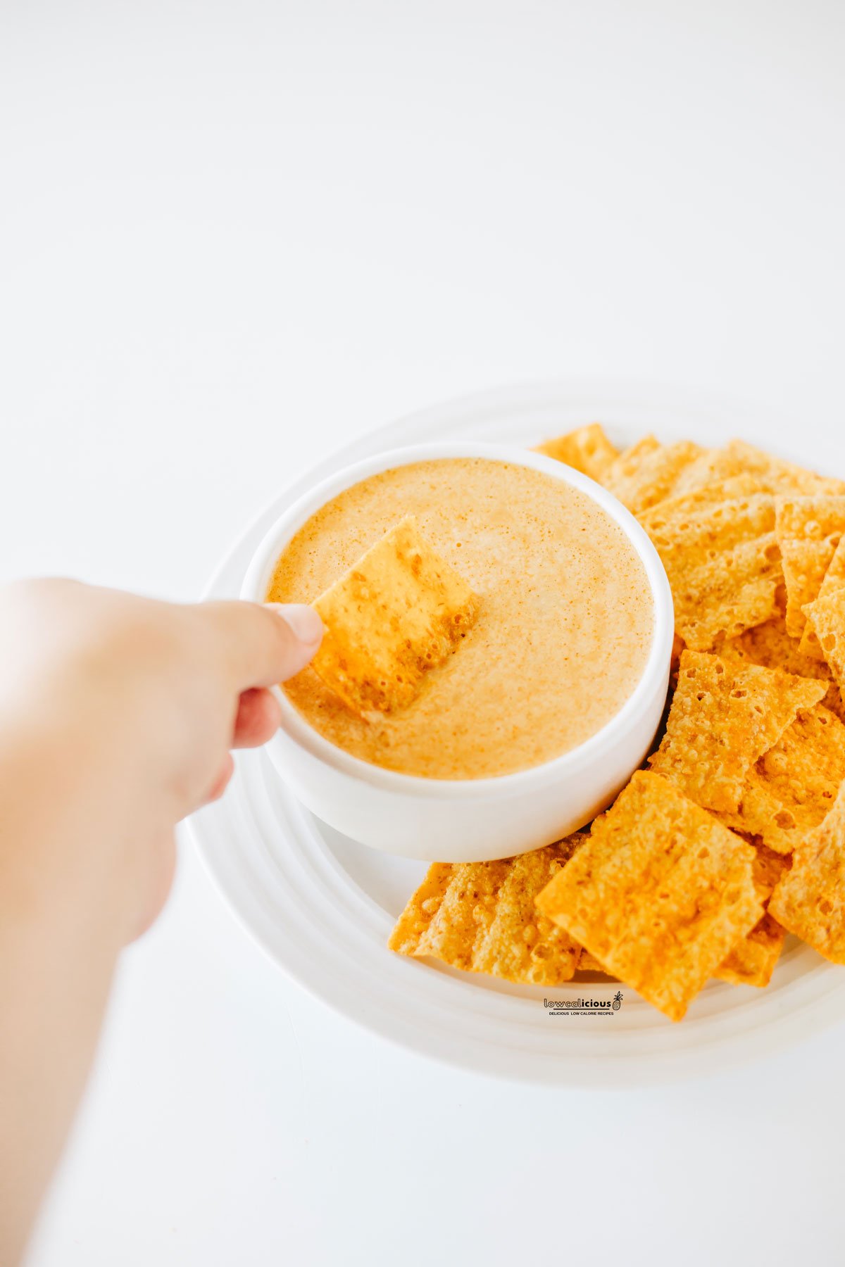 a hand holding an orange Sun Chip and dipping it into prepared Viral TikTok Cottage Cheese Queso Dip