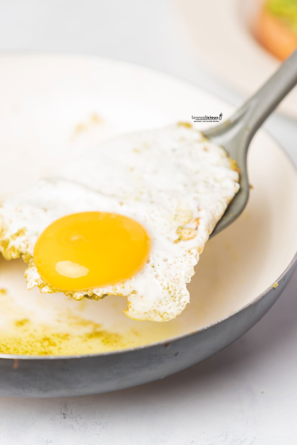 a fried pesto egg being lifted out of a nonstick skillet with a spatula to serve Pesto Eggs