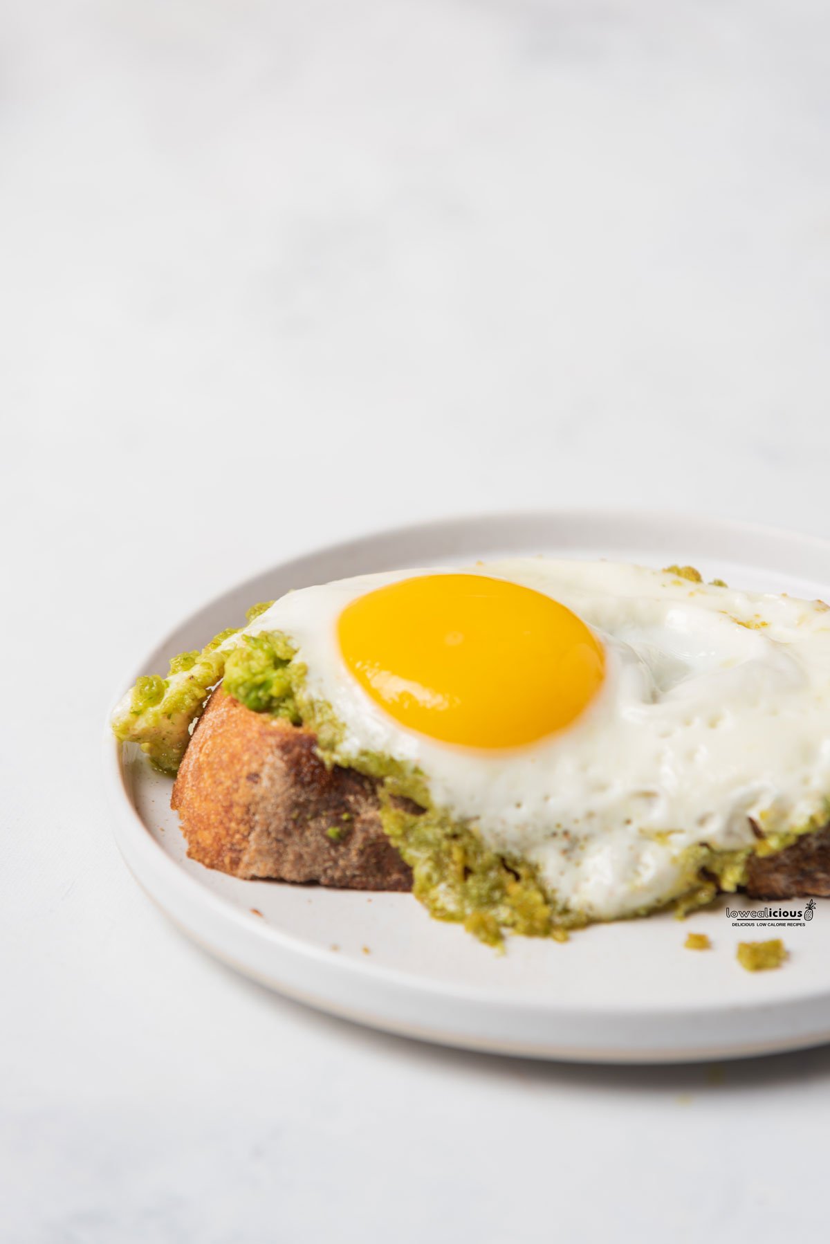 cooked Pesto Eggs recipe (Viral TikTok Recipe) served on top of smashed avocado on a slice of sourdough bread on a round white plate