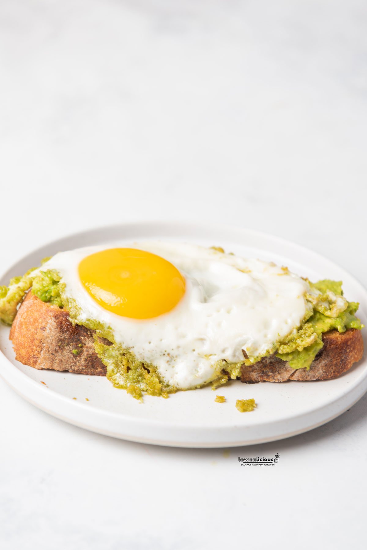 Easy Pesto Eggs (Viral TikTok Recipe) cooked and served on top of smashed avocado on a slice of sourdough bread on a round white plate