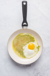 a nonstick skillet with pesto and an egg cooking in it to make Pesto Eggs (Viral TikTok Recipe)